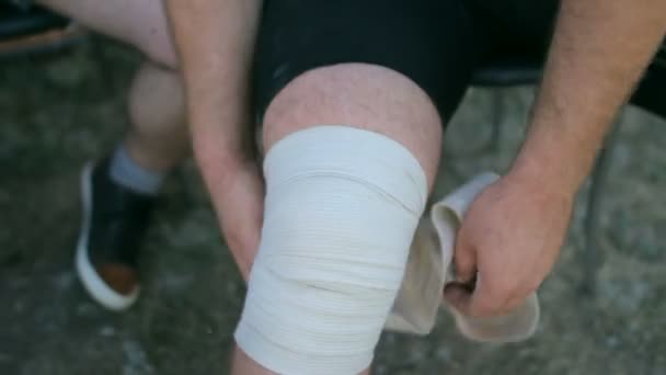 Спортсмен после соревнований снимает повязки на коленях — стоковое видео