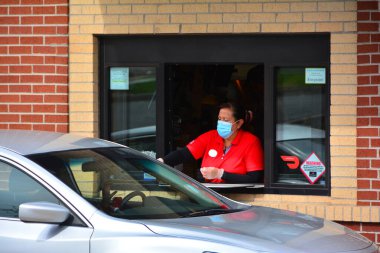 Chick-fil-A 'da kimliği belirsiz bir fast food işçisi. Maske ve eldiven takıyor ve vitrindeki müşteriye yemek servisi yapıyor.. 