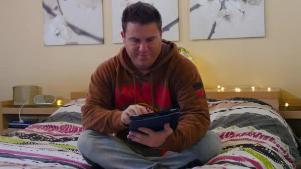 Uomo che usa tablet seduto sul letto nella sua camera da letto. 4K . — Video Stock