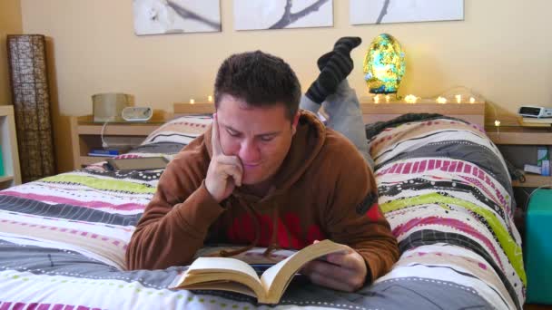 Uomo che legge un libro sdraiato sul letto in camera da letto — Video Stock