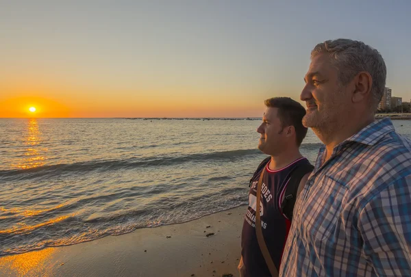 Padre e hijo viendo una hermosa puesta de sol en la playa Fotos De Stock Sin Royalties Gratis