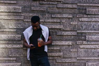 Afrikalı Amerikalı bir elinde smoothie tutarken diğer elinde kendi telefonu vardı.