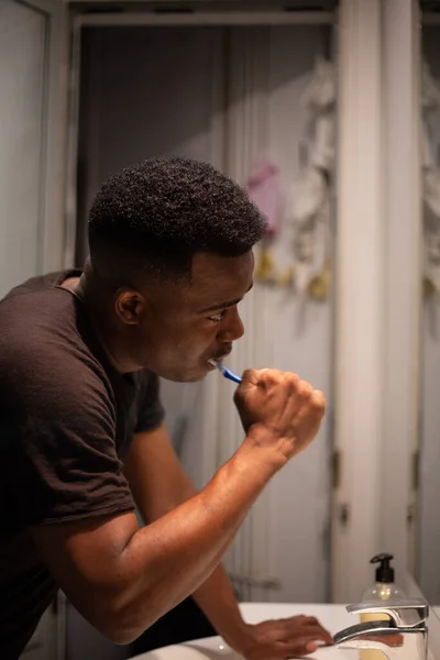 Afrikalı Amerikalı, aynanın önünde dişlerini fırçalarken dişlerini fırçalarken kendini izliyor.