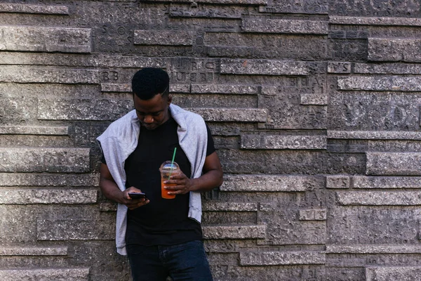 Afrikalı Amerikalı bir elinde smoothie tutarken diğer elinde kendi telefonu vardı.