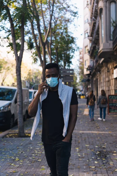 Barcelona caddelerinde telefonla konuşurken, Covid-19 maskeli Afro-Amerikalı.