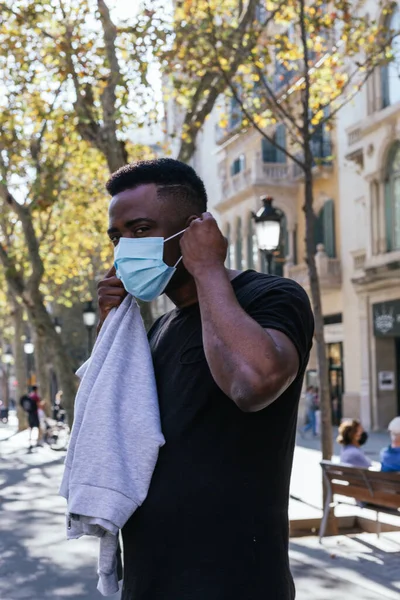 Afrika kökenli Amerikalı, maskesini Barselona sokaklarında takıp doğrudan kameraya bakıyor.