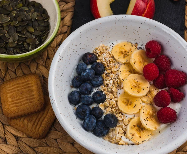 Balkabağı çekirdeği, kurabiye ve dilimlenmiş elmadan oluşan fitness kahvaltısı. Ayrıca içinde beyaz bir kasede bir kase meyve var.