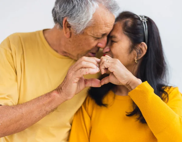 Tanımlanamayan yaşlı çift öpüşürken elleriyle kalp yapıyor.