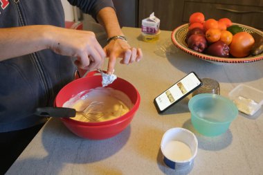 İnternetteki talimatları takip ederek peynirli kek malzemelerini karıştıran beyaz bir kadın şef.