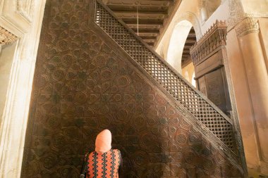 Ahmad ibn tulun camiinin içindeki oyulmuş ahşap minibarı ve mihrab 'ı izleyen kadın.