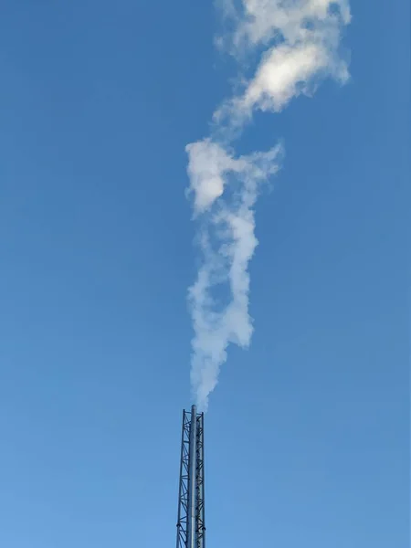 Emissions in the form of white smoke into the atmosphere from a metal pipe of a stationary block-modular boiler house against a blue sky. Environment, atmosphere. Global warming.