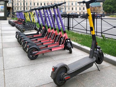 Şehir caddesinde arka arkaya park etmiş elektrikli scooterlar kiralanmış. Hareket için ekolojik taşıma.