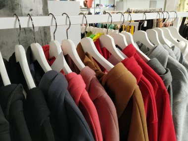 Mağazadaki gösteri standında çeşitli renklerde moda giysiler seçim ve satın alma için askılara asılıyor. Marketten alışveriş. Modern teknolojik ve günlük giysiler.