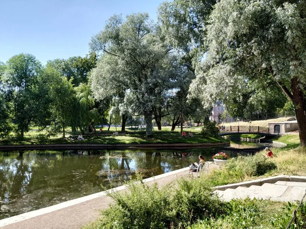 On a summer day, people relax in the garden. View of the trees, pond, bridge in the Yusupovsky Garden in the old center of St. Petersburg. Recreation places for residents of the city of St. Petersburg. Summer vacation of citizens.