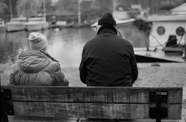 Elderly couple with their backs turned, sitting on a bench looki