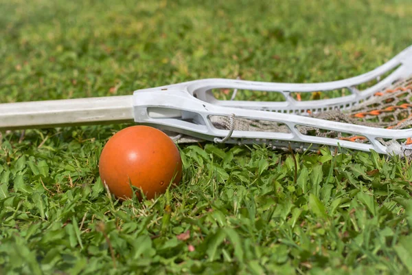 Women\'s lacrosse stick laying on a lacrosse field with yellow lacrosse ball