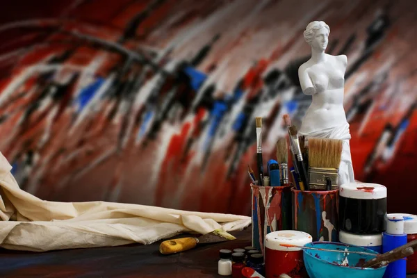 絵画の異なる色で覆われたカップの絵筆のクローズアップショットとアートスタジオのヴィーナス像 — ストック写真