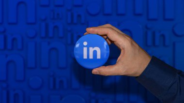 Odaklanmamış mavi arka planda linkedin parlak rozetini tutan bir el.
