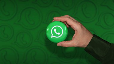 Odaklanmamış koyu yeşil arka planda bir Whatsapp rozetini tutan bir el.