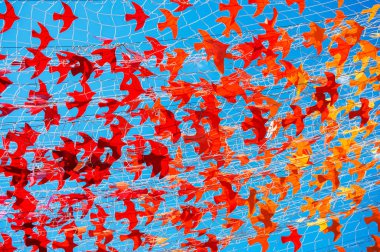 Kağıt kırmızı ve turuncu kuşlar mavi gökyüzüne karşı örgü örerler. Zor zamanlarda umut ve iyileşmenin sembolü..