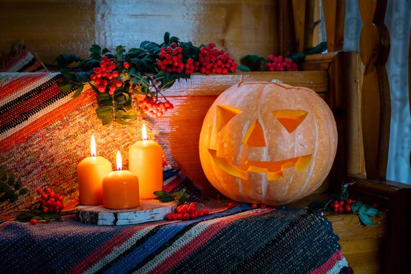 Halloween card. Happy Halloween. Halloween concept in rustic style. Jack's lantern from pumpkin and candles on a wooden staircase. Rowan bunches lie around. Autumn orange concept. Pumpkin with a cut out muzzle. Copy space. Selective focus.