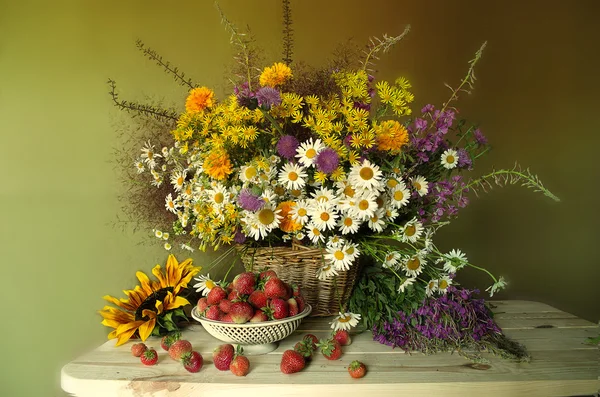 Csendélet bogyós gyümölcsök és virágok. Vörös, érett szamóca és egy csokor vadvirágok és napraforgó . — Stock Fotó
