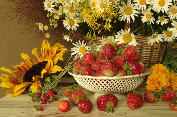 Çilek ve çiçeklerle natürmort. Kırmızı, olgun çilek ve kır çiçekleri ve ayçiçeği bir buket .