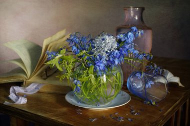 Still life with blue, spring primroses and an old book in the background.