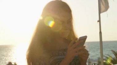 Genç kız smartphone ile sahilde. Günbatımı