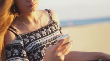 Genç kız smartphone ile sahilde. Günbatımı