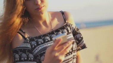 Genç kız smartphone ile sahilde. Günbatımı