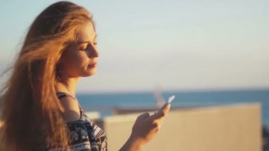 Genç kız smartphone ile sahilde. Günbatımı