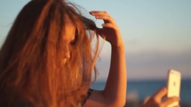 Genç kız smartphone ile sahilde. Günbatımı