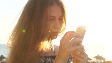 Genç kız smartphone ile sahilde. Günbatımı