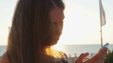 Genç kız smartphone ile sahilde. Günbatımı