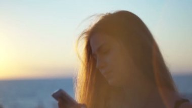 Genç kız smartphone ile sahilde. Günbatımı