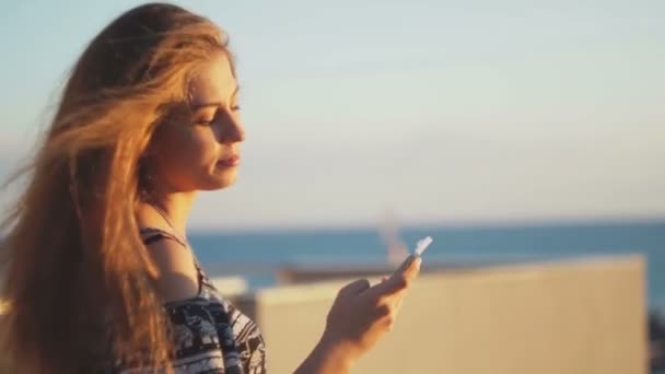 Chica joven en la playa con su teléfono inteligente. Puesta de sol — Vídeo de stock
