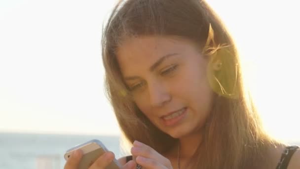 Jeune fille sur la plage avec votre smartphone. Coucher de soleil — Video