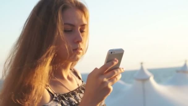 Jeune fille sur la plage avec votre smartphone. Coucher de soleil — Video