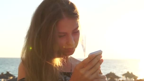 年轻的女孩，在沙滩上与您的手机。日落 — 图库视频影像