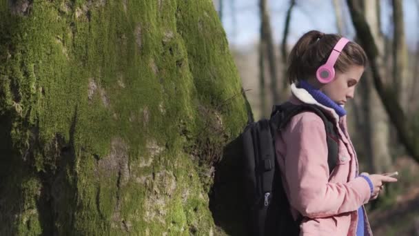 若い女の子がスマホを持った木の近くに立っている。自然界における自己分離 — ストック動画