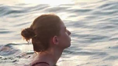 Gün batımında denizde yüzen genç bir kızın yakın plan portresi.