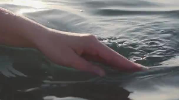 Nahaufnahme einer Frauenhand berührt sanft Oberflächenwellen des Meeres im Sonnenuntergang — Stockvideo