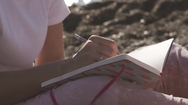 Menina faz anotações em seu caderno enquanto na praia em um dia ensolarado — Vídeo de Stock