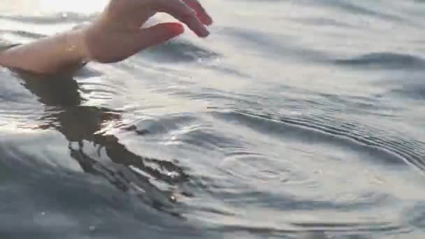 Close up of a womans hand is gently touching surface waves of the sea in sunset — Stock Video