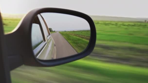 View from the car window into the rear view mirror. Sunset, steppe, Dirt road — Stock Video