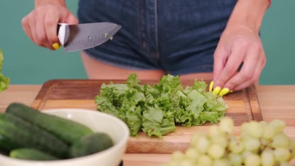 Обрізаний знімок жінки в шортах для різання салату на обробній дошці на зеленому фоні — стокове відео