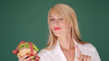 Kadın hamburgere bakıyor ve yeşil arka planda abur cuburu yasaklıyor.