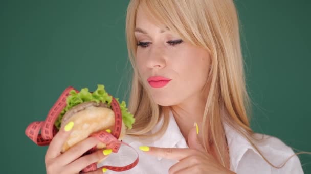 Kvinde kigger på burger og forbyder junk food på grøn baggrund – Stock-video