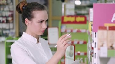 Kadın bir eczacı raftaki bazı ürünlere bakıyor.